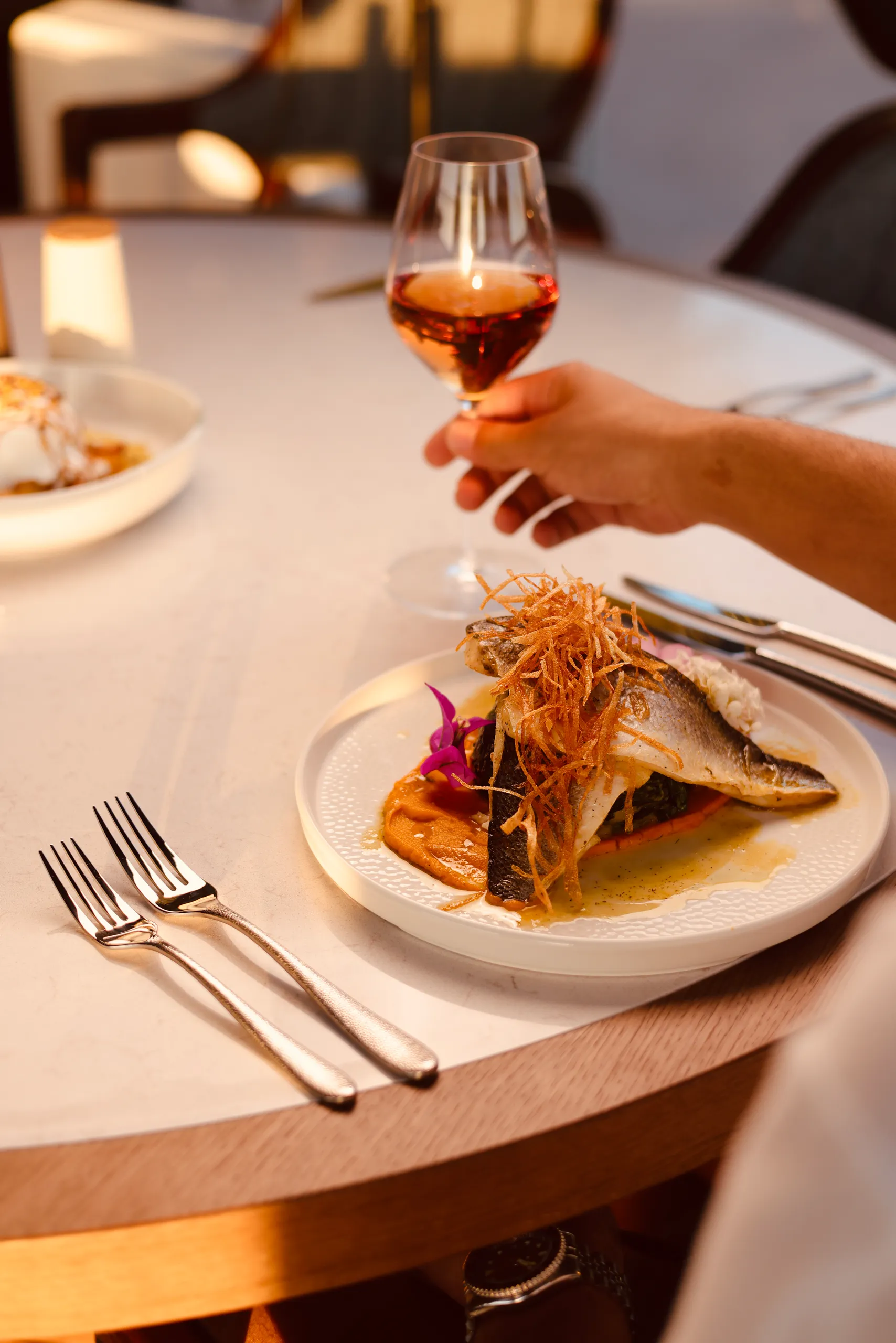A fire-led main course at KALO, plated with a glass of wine.